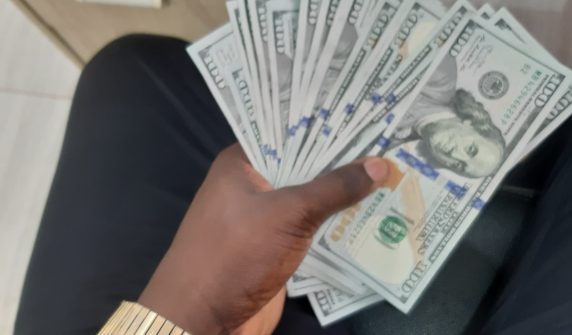 ہاتھ میں امریکی سو ڈالر کے نوٹ — dollar rate today کے مطابق انٹربینک میں ڈالر 276.87 روپے
